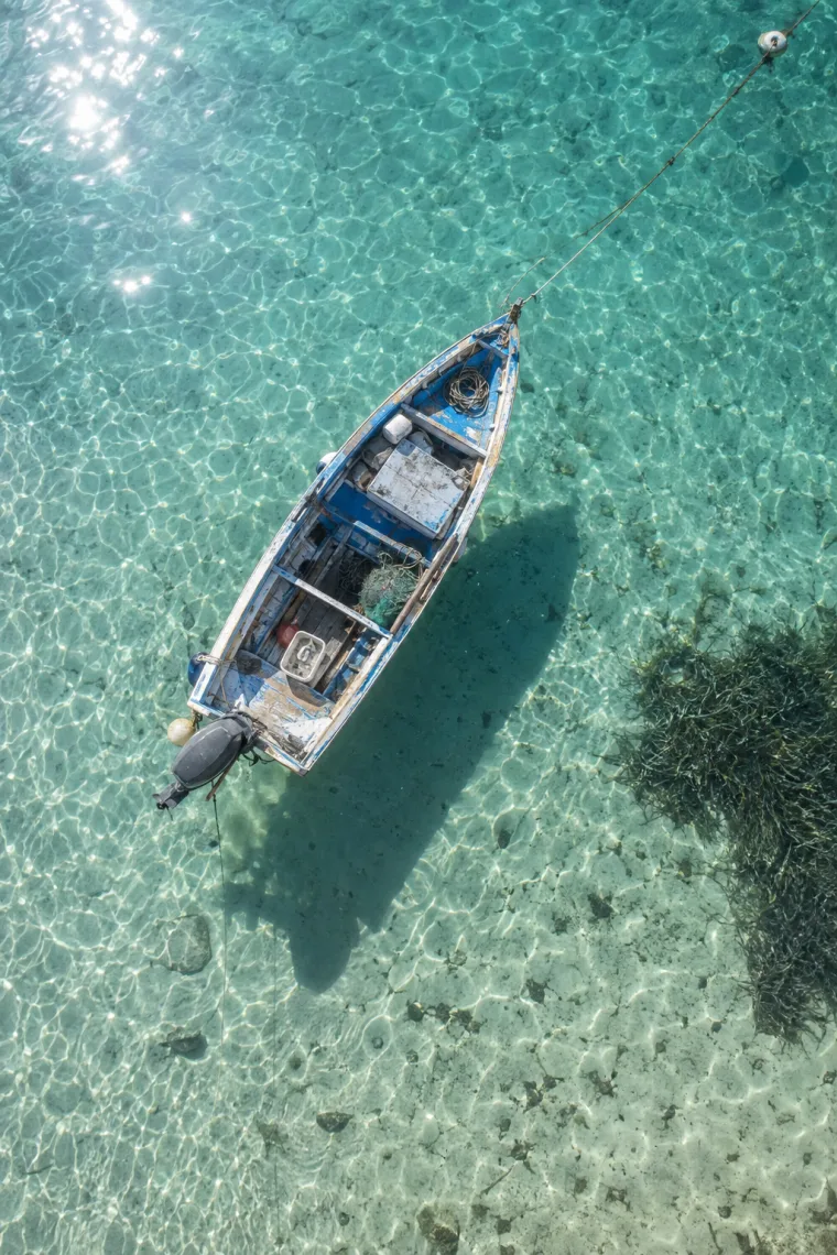 Candidate 1: a white-and-blue wooden fishing boat seen from above in shallow turquoise water