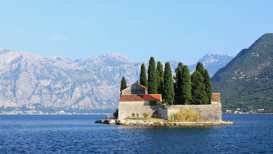 Candidate 2: a small island with a stone church and cypress trees in a mountain-ringed bay